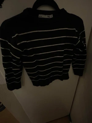 Svart stickad tröja med vita ränder - Snygg svart stickad tröja med tunna vita horisontella ränder. Tröjan har rund halsringning och långa ärmar.