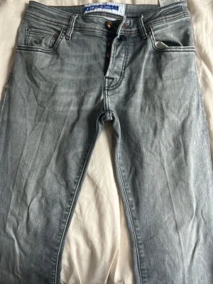 Ljusblå jeans från Jacob Cohen - Snygga ljusgråa jeans från Jacob Cohen med klassisk femficksmodell och raka ben. Jeansen har diskreta slitningar och kontrastsömmar, samt en läderpatch med logga bak i midjan. Tillverkade i mjuk denim som ger en skön passform.