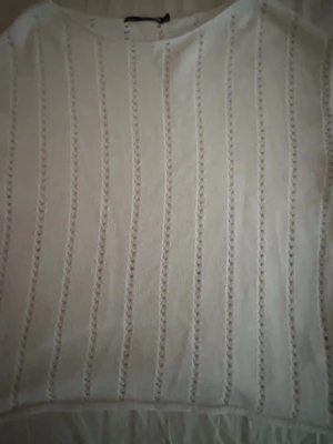 Vit stickad tröja med hålmönster - Säljer en vit stickad tröja med lång ärm och snyggt hålmönster i vertikala ränder. Tröjan har rund halsringning och är tillverkad i ett mjukt material som känns skönt mot huden. Perfekt för lager-på-lager och en stilren look.