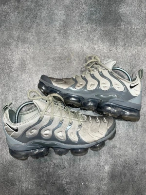 Nike VaporMax Plus - Nike Air VaporMax Plus i grå/silver. Storlek 42,5.  Mycket bra skick överlag. Finns en liten slitning på högerskon vid stortån (sista bilden)