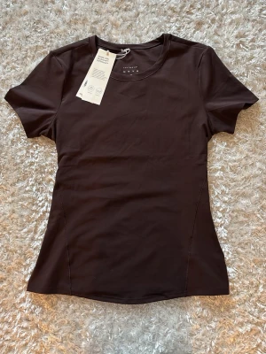 Mörkbrun träningst-shirt  - Snygg mörkbrun träningstshirt. Stretchigt material och säljer den pågrund av att den var slut i min storlek och testade M istället men den blev lite stor. Älskar dock färgen och modellen!!! Prislappen sitter kvar och den är helt oanvänd