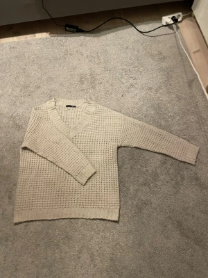 Stickad tröja - Mysig beige/kräm färgad stickad tröja med v-ringad hals och grovstickat mönster. Tröjan har långa ärmar och ribbade muddar vid ärmslut och nederkant. Super skön och stiks inte utan är mer i ett bomullmjukt tyg. Köpt på lager 157 och är i storlek M.