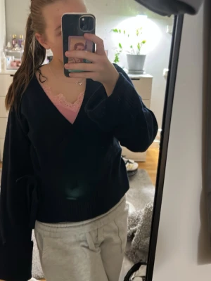 Mörkblå omlottkofta med v-ringning - Säljer en mörkblå omlottkofta med djup v-ringning och breda ärmar. Koftan har en ribbstickad nederkant och är perfekt att slänga över en topp. Materialet ser ut att vara mjukt och stickat.