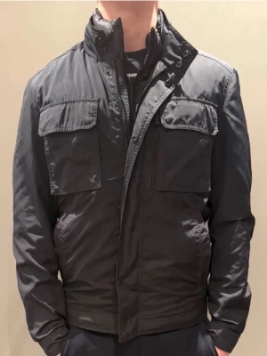 Field Jacka Massimo Dutti - Snygg marinblå fieldjacka med hög krage och flera praktiska fickor framtill. Jackan har dragkedja och tryckknappar, samt långärmad design. Perfekt för våren. Inga hål eller flaws.