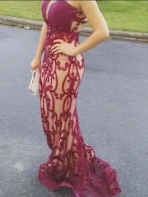 Vinröd långklänning med spetsdetaljer - Säljer en vinröd långklänning med transparenta partier och broderade spetsdetaljer. Klänningen är axelbandslös och har en figurnära passform med vacker släp. Perfekt för bal eller festliga tillfällen.