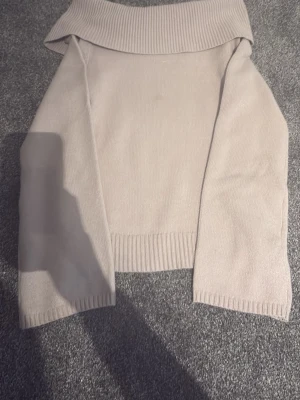 Beige off shoulder stickad tröja - Säljer en beige stickad tröja med bred off shoulder-krage och långa ärmar. Tröjan har ribbade muddar vid ärmslut och nederkant, och är i mjukt material som känns skönt mot huden. Perfekt för dig som gillar en stilren och enkel look.