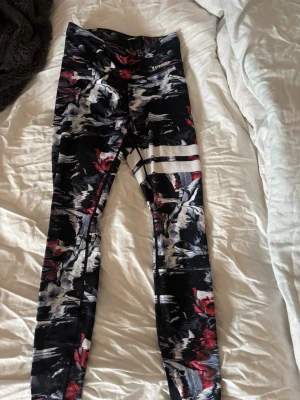 Mönstrade leggings från Stronger - Säljer ett par snygga tights från Stronger med svart, vitt och rött abstrakt mönster. De har hög midja och sitter tight, perfekta för träning eller chill. Materialet är stretchigt och följsamt för bästa komfort.