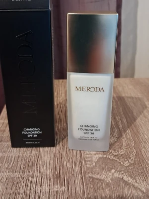 Meroda Changing Foundation SPF 30 - Foundation från Meroda i en elegant glasflaska med guldigt lock. Changing Foundation SPF 30 anpassar sig till ljusa och medelstora hudtoner för en naturlig finish. Innehåller 30 ml och ger skydd mot solen. Perfekt för dig som vill ha en smidig basprodukt.