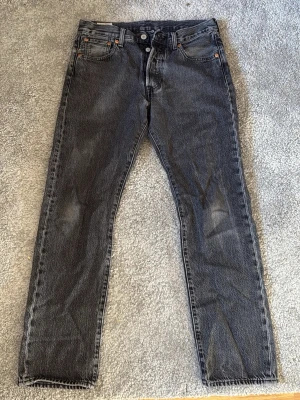 Levi's 501 - Säljer ett par svarta raka jeans från Levi's Premium med klassisk femficksmodell och knappgylf. Jeansen har en tvättad look och är tillverkade i slitstarkt denimtyg. Perfekta för dig som gillar en tidlös och avslappnad stil. Modellen är 501. Storlek 30/30