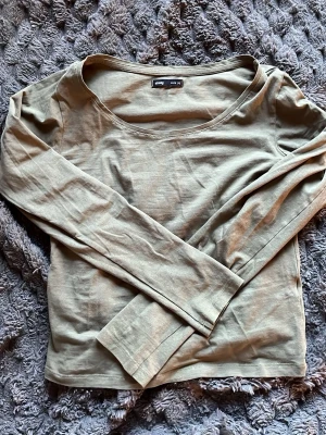 Olivgrön långärmad topp  - En enkel och stilren olivgrön långärmad topp . Toppen har rund halsringning och är tillverkad i mjuk bomull, perfekt att matcha med jeans eller kjol för en avslappnad look.