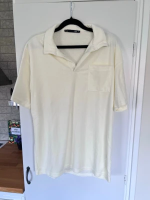 Krämvit frotté t-shirt med krage - En crémevit skjorta i frottématerial, storlek S. Korta ärmar,  krage och en bröstficka. Aldrig använd.