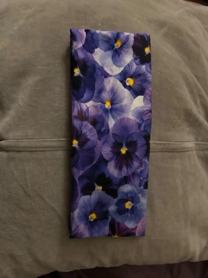 Lila hårband med violmönster - Snyggt hårband med intensivt violmönster i olika nyanser av lila, blått och inslag av gult. Tunn och mjuk, perfekt att styla till jackan eller runt halsen för en färgklick. Blommigt motiv som ger en fräsch och ungdomlig vibe.