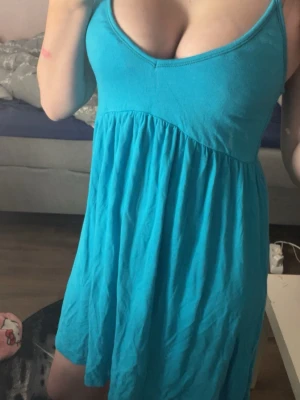 Turkos kort klänning med smala axelband - Säljer en turkos kort klänning med smala axelband och v-ringning. Klänningen har en luftig passform och är tillverkad i ett mjukt bomullsliknande material. Perfekt för varma dagar och enkel att styla med accessoarer.