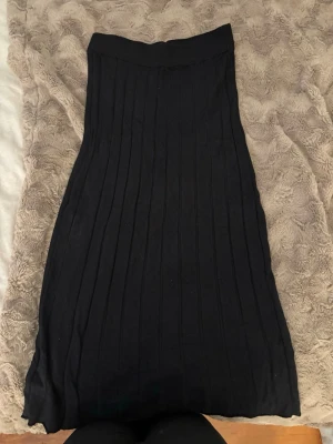 Svart långkjol från Stories - Säljer en svart långkjol från Stories i storlek S. Kjolen har en ribbad struktur och är i ett mjukt, stretchigt material som sitter snyggt i midjan. Perfekt att styla med en croppad topp eller stickad tröja för en trendig look.