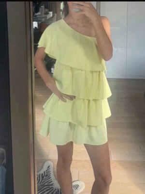 Ny populärt Zara  Gul one shoulder volangklänning - Säljer en ljusgul kortklänning med one shoulder och flera lager volanger. Klänningen har en lös passform och är perfekt för sommarens varma dagar. Materialet känns lätt och luftigt.