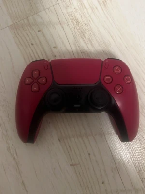Röd PlayStation 5 DualSense handkontroll - Säljer en snygg röd PlayStation 5 DualSense handkontroll från Sony. Handkontrollen har en modern design med svarta detaljer och klassiska PlayStation-knappar. Tillverkad i plast och passar perfekt för gaming på PS5.