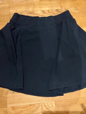 Svart kortkjol i bomull - En enkel svart kortkjol i mjukt bomullstyg. Kjolen har en lätt utsvängd form. Lapp saknas! Jag TROR den är från hm, och jag upplever den som storlek S! (inte säker)