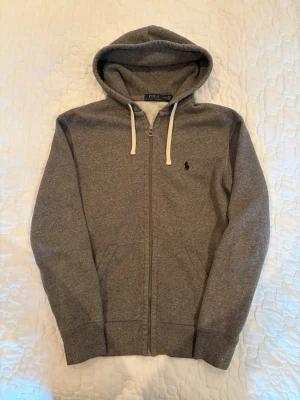 Ralph Lauren Zip Hoodie - Säljer denna riktigt feta Ralph Lauren Zip hoodien i grå. Hoodien är i superfint skick. Passar till allt. Skick - 9/10 Storlek - M Försöker skicka samma dag annars så snabbt jag kan! Skriv om du har fler frågor!