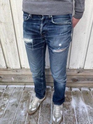 Our Legacy ”First Cut” med Slitningar - Ett par extremt snygga jeans från Our Legacy med öppna slitningar! Mycket fin wash på dessa, utsydda från W29 till W30. Sista bilden visar att främre delen av gylfen förstärkts med extra tyg. Hör av dig bid frågor! Mått: Ytterben - 97 cm,  Midja - 42 cm, Benslut - 17.5 cm