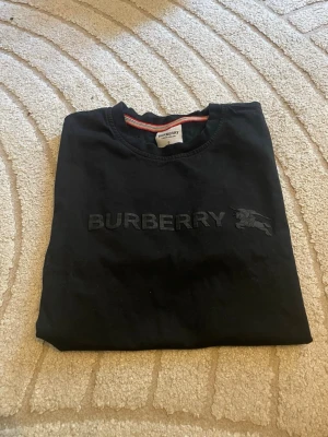 Svart Burberry t-shirt i bomull - Snygg svart t-shirt från Burberry med diskret broderad logga och ikon på bröstet. Klassisk rund halsringning och korta ärmar. Tillverkad i mjuk bomull som känns skön mot huden. Perfekt för dig som gillar stilrena och exklusiva plagg. Använd gärna köp nu
