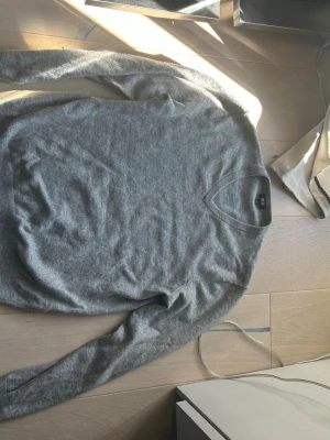 Grå stickad tröja med V-ringning  - Mjuk och stilren grå stickad tröja från Uniqlo med V-ringad hals. Tröjan är ny och säljs pga att jag växt ut ur den, tillverkad i 100% Kashmir, nypris: 1199kr. Mitt pris: 499. Skriv för funderingar👍