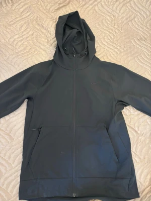 Svart hoodie från Nike med dragkedja - Säljer en svart hoodie från Nike med hel dragkedja framtill och två stora fickor. Hoodien har justerbar huva med snören och diskret Nike-logga på bröstet. Tillverkad i ett mjukt och slitstarkt material som passar perfekt till streetwear.