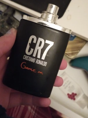 CR7 Game On parfym - Stilren parfymflaska i svart med silverdetaljer och texten 'CR7 Game On' från Cristiano Ronaldo. Flaskan har en modern, sportig look och är enkel att använda tack vare sprayfunktionen. Perfekt för dig som gillar fräscha och energiska dofter.