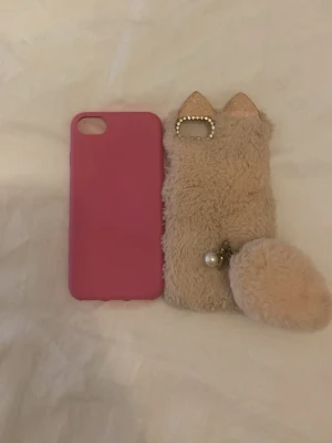 Två mobilskal, rosa & fluffigt beige - Säljer två mobilskal: ett enkelt rosa silikonfodral och ett beige fluffigt skal med kattöron, pärldetaljer och en stor boll. Det fluffiga skalet har även glittriga öron och pärlberlock. Perfekt för dig som vill ha något gulligt och unikt till mobilen.