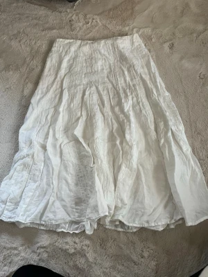 Vit långkjol i linne från Ricshaw - Säljer en vit långkjol från Ricshaw Torino i luftigt linne. Kjolen har en flowy passform med fina sömdetaljer och dragkedja i sidan.