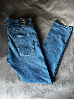Blå jeans från Replay - Blå jeans från Replay med klassisk femficksdesign och raka ben. Jeansen är i modellen anbass, slim fit, (30/32). Perfekta för dig som gillar stilrena och tidlösa jeans.