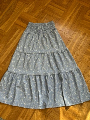 Blå långkjol med blommigt mönster - Säljer en ljusblå långkjol med små vita blommor och bred smock i midjan från Gina tricot💕💕 Kjolen har volanger och är luftig💕💕I mycket bra skick💕💕Nypris är 300 kr, jag säljer den för 150 kr💕💕Hör av er vid intresse💕💕
