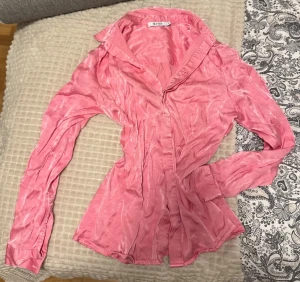 Rosa sammetsblus från NA-KD - Trendig rosa blus från NA-KD i mjukt sammetsmaterial. Figurnära modell med långa ärmar, bred krage och knäppning framtill. Perfekt för dig som vill ha en statement piece i garderoben.