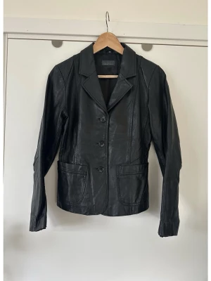 Svart skinnjacka / kavaj i 100% äkta läder, storlek 38 - Svart skinnkavaj / jacka i 100% äkta läder från ROCK AND BLUE i storlek 38. Tidlös modell med klassisk krage och figurnära passform. Stilrena fickor och knappar framtill. Perfekt för dig som vill ha ett plagg som kommer funka säsong efter säsong. Superfin, men tyvärr för liten för mig nu. Nypris 2600:-. Mycket fint skick.   (Skickas helst, men kan även hämtas i Stockholm vid behov)