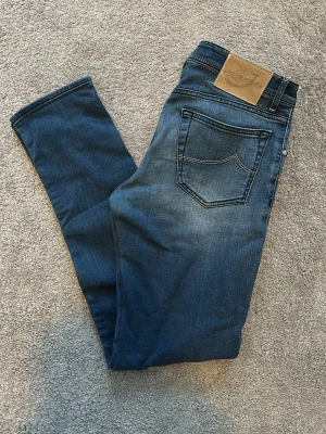 Jacob Cohen 622 - Säljer ett par blåa jeans från Jacob Cohen modell 622 med klassisk femficksdesign. Jeansen har en läderpatch med logga bak i midjan och kontrastsömmar. Perfekta för dig som gillar en smal passform och tidlös stil. Storlek 33, Midja: 42 cm, Ytterbenslängd: 106 cm. Mycket bra skick på jeansen!