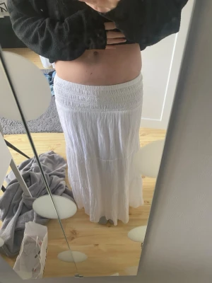 Vit långkjol med resårmidja - Luftig vit långkjol med bred resår i midjan som ger en bekväm passform. Kjolen har ett lätt, flödande tyg och enkel design som passar perfekt till sommardagar. Stilren och enkel att matcha med olika toppar. Storlek 164.