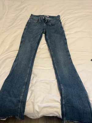 Blå bootcut jeans med broderade fickor - Säljer ett par klassiska blå bootcut jeans med snygga broderade detaljer på bakfickorna. Jeansen har låg midja