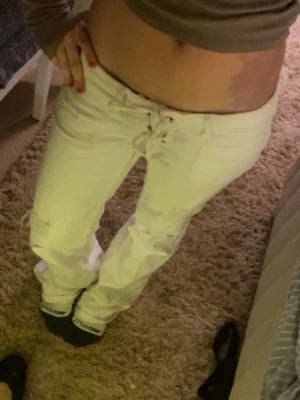 Vita jeans med snörning - Säljer ett par vita bootcut jeans med snörning i midjan och slitna detaljer på benen. Jeansen har hög midja och vida ben. Passar både M men också S💕