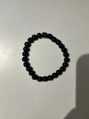 Svart pärlarmband i matt finish - Stilrent svart armband med runda, matta pärlor trädda på elastisk tråd. Perfekt för dig som gillar minimalistiska accessoarer med en clean look. Passar både ensam eller i kombination med andra armband.