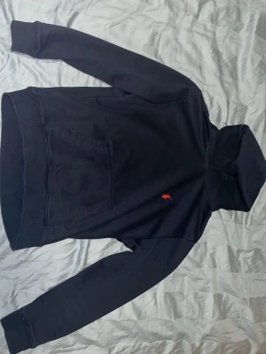 Ralph Lauren - Klassisk marin blå hoodie från Polo Ralph Lauren med röd broderad logga på bröstet. Hoodien har huva och en stor magficka framtill. Tillverkad i mjukt bomullsmaterial som är skönt mot huden och lite tunnare material som är perfekt nu inför sommaren. Perfekt för en avslappnad och stilren look. Storlek M i barn men sitter ungefär som en XS eller S.