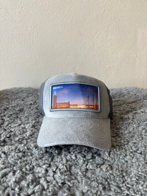 Revenite popup keps - Snygg grå keps från Revenite med mesh på sidorna och ett broderat motiv av Stockholms stadshus framtill. Perfekt accessoar för dig som gillar stilrena detaljer och stadsmotiv. Nypris 699kr från Revenites egna butik, mitt pris endast 399kr men kan diskuteras vid snabb affär 