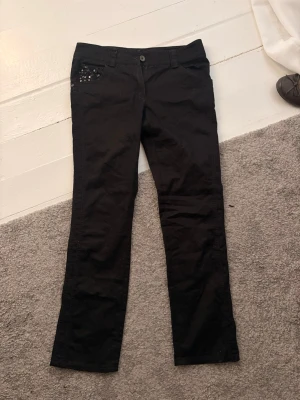 Svarta jeans med plajetter - Säljer ett par svarta jeans med raka ben och coola paljetter på ena framfickan. Jeansen har normal passfrom, knappgylf och klassisk femficksdesign. Perfekta för dig som vill ha en edgy look till vardags.