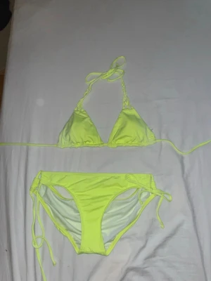 Neongul bikini med knyt - Säljer en snygg neongul bikini med trekantsöverdel och knyt i nacken samt på sidorna av underdelen. Bikinin har en enkel och fräsch design som verkligen poppar på stranden. Perfekt för dig som vill sticka ut i sommar! Det står ingen storlek men jag gissar på S.