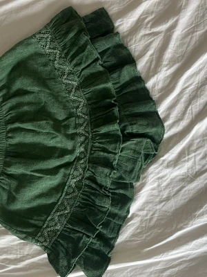 Grön volangkjol  broderi med inbyggda shorts - Supersöt grön kortkjol med dubbla volanger och broderade detaljer. Kjolen har resår i midjan för skön passform och är gjord i ett mjukt tyg som känns luftigt. Perfekt för dig som gillar en bohemisk och avslappnad stil. Har även insydda short under