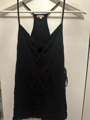 Svart linnetopp med cut out från Bikbok - Svart linnetopp från Bikbok med smala axelband och en snygg cut out-detalj framtill. Toppen har v-ringning och ärmlös design, perfekt för en trendig och avslappnad stil.