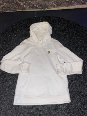 Vit hoodie från Lyle & Scott - Säljer en clean vit hoodie från Lyle & Scott med klassisk gul logga på bröstet. Hoodien har en stor magficka. Perfekt basic-plagg för dig som gillar enkel och stilren streetwear. Materialet är mjukt och skönt bomullstyg. Kom med eventuella frågor!