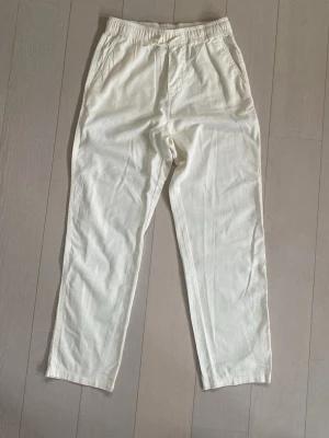 Vita linnebyxor  - Säljer ett par vita linnebyxor från H&M med avslappnad passform och resår i midjan. Byxorna har raka ben och sidofickor, perfekta för en chill och stilren look. Tillverkade i lätt och luftigt linnematerial.