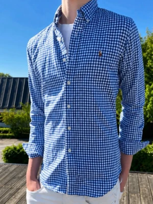 Blårutig skjorta från Ralph Lauren - (Modellen är 185cm och väger 75kg)Klassisk blårutig skjorta från Ralph Lauren med button-down krage och långa ärmar. Skjortan har vita knappar framtill och en liten broderad logga på bröstet. Tillverkad i bomull för en bekväm känsla och snygg passform.