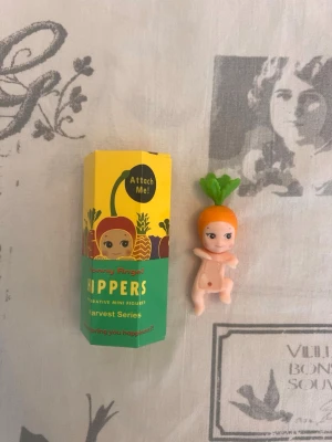 Sonny Angel Hippers morotsfigur - Säljer en Sonny Angel Hippers mini figur från Harvest Series. Figuren föreställer en söt baby med morotshatt och gröna blad. Förpackningen är färgglad med illustrationer av olika frukter och grönsaker. Perfekt som dekoration eller samlarobjekt.Helt ny oöppnad 