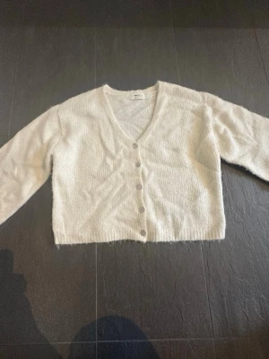 Vit kofta från Gina Tricot i storlek XS - Mysig vit kofta från Gina Tricot i ullblandning. Koftan har v-ringning, långa ärmar och knäppning med fyra knappar framtill. Perfekt för lager på lager och enkel att styla till olika outfits.