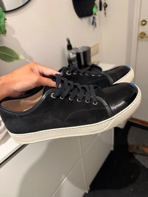 Svarta sneakers med vit sula - Stilrena svarta sneakers med vit sula och svarta skosnören. Ovandelen är i mocka och tåpartiet i lack för en snygg kontrast. Klassisk låg modell som passar till det mesta. Perfekta för dig som gillar enkel och clean stil. Skorna är knappt använda därav i väldigt bra skick!  Påsen till skorna medföljs 
